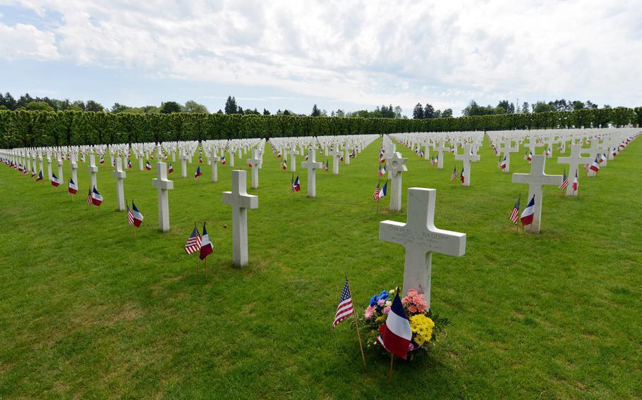 American cemetery in France with flags decorating the graves set in a manicured lawn.