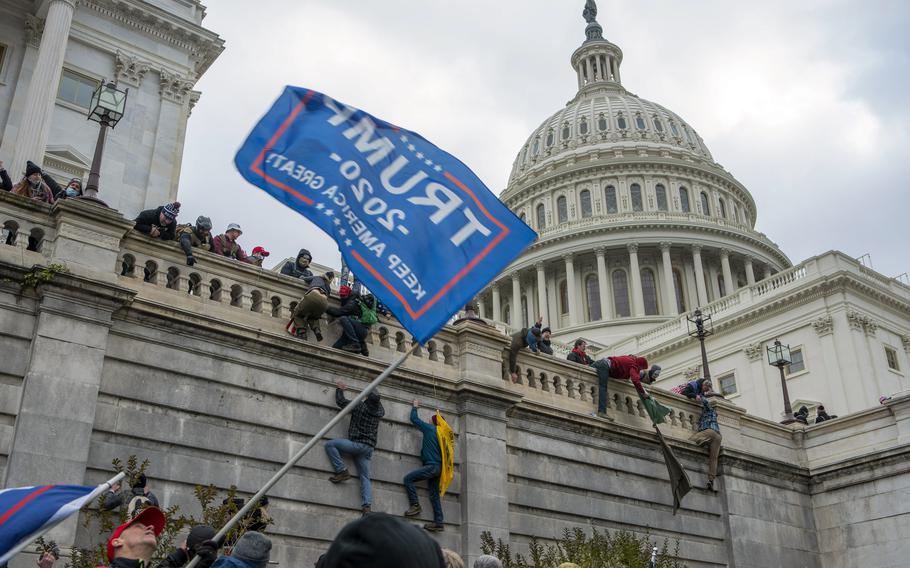 People climb the wall of the U.S. capitol and wave a flag that says Donald Trump.