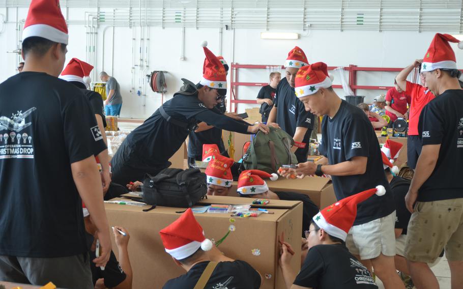 Airmen and other volunteers wearing red Christmas hats prepare boxes for Operation Christmas Drop.