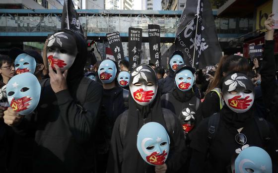 FILE - Pro-democracy protesters wear masks depicting the hand with Chinese Communist party emblem covering their mouth during a march on a street in Hong Kong on Dec. 8, 2019. (AP Photo/Mark Schiefelbein, File)