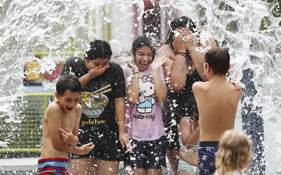 Yezica Jimenez, 16, from left, Luzmaria Celis, 13, and Sandra Cortez stand under a water barrel at the splash pad inside Waterfront Park in Louisville, Ky., on Tuesday, June 18, 2024. 
