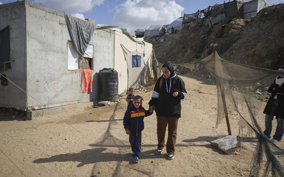 A woman wearing a head covering walks outside holding hands with her young son.