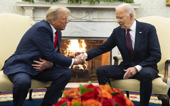 Joe Biden and Donald Trump shake hands while seated in front of a fireplace in the Oval Office of the White House.