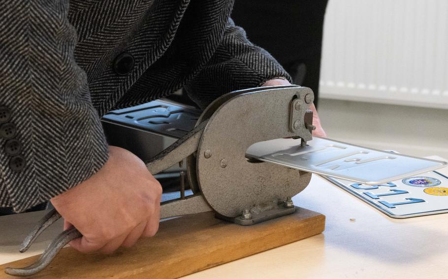 A customer at a vehicle registration office in Germany punches holes in a new license plate.