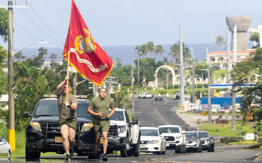 Two Marines run on the street with cars behind them, while one carries the Corps flag, in Hagåtña, Guam, Nov. 6, 2024.