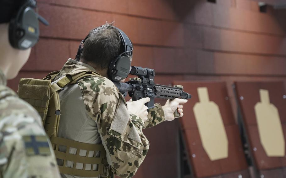 A man in camoflauge is seen aiming a rifle in an indoor shooting range.