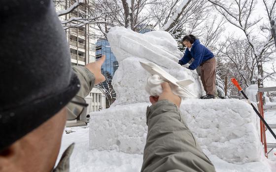 Chief Enrico Dagsindal holds a small model of an F-35C Lighting II while Petty Officer 1st Class Caroline Lui works on the snow sculpture for the 75th Annual Sapporo Snow Festival. 