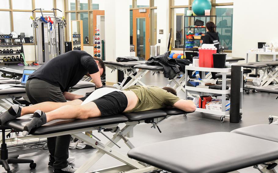 A guy standing provides treatment to another guy lying on a table.