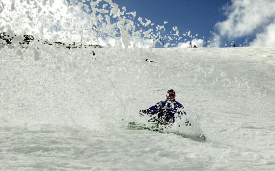 A snowboarder kicks up a curtain of snow as he slides down a slope.