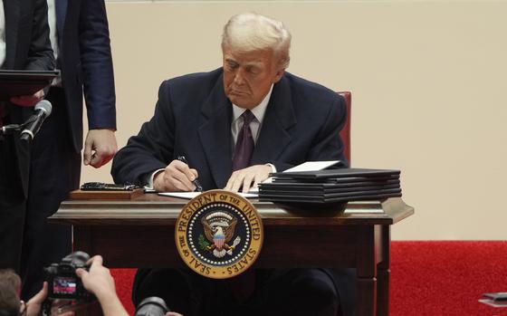 President Donald Trump sits at a desk and signs papers.