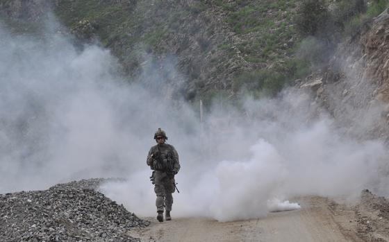 A soldier from COP Monti walks on the road along the Kunar River Valley after a smoke grenade was set off to mark the site of a suspected bomb that was spotted in the ground.