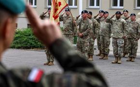 A Polish land forces officer and American soldiers of U.S. Army Garrison Poland salute during the Polish national anthem during the garrison’s change of command ceremony June 28, 2024, at Camp Kosciuszko in Poznan.