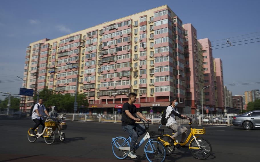 Chinese riding bicycle pass by a local business building the in background in Beijing, China, Friday, June 28, 2024. Surveys of Chinese factory managers showed a mixed outlook for the world's second-largest economy in June, with growth steady but not picking up much steam. 