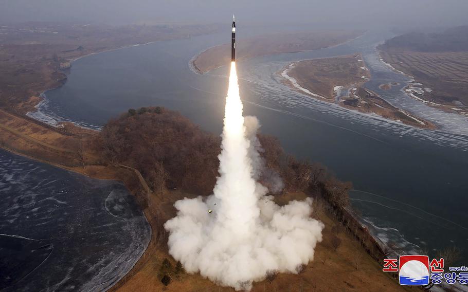 A ballistic missile, seen from a distance, rises into the sky with a line of fire and smoke trailing underneath it.