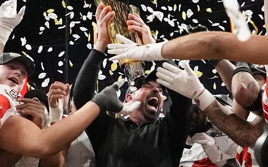 A football coach holds up a trophy and cheers with his players.