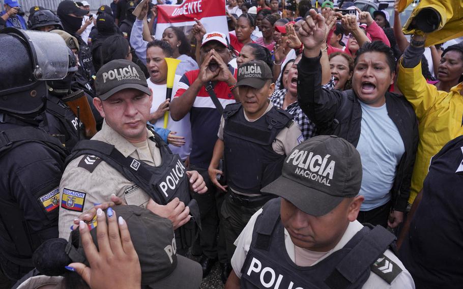 Police officers are seen in front of a mass of protesters who are chanting or shouting.