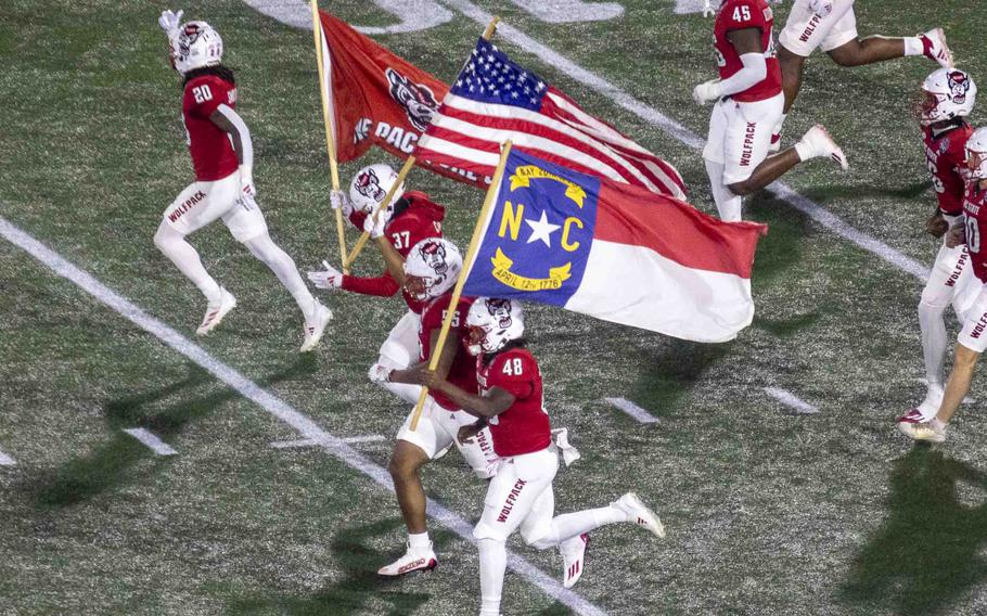 North Carolina State football players run across the football field carrying flags.