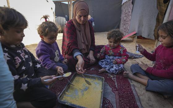 A woman and four small girls sit around a pan of lentils in a refugee camp.