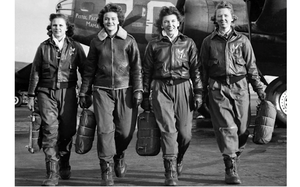 A black and white photo of four women in WWII-era uniforms carrying luggage.