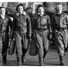 A black and white photo of four women in WWII-era uniforms carrying luggage.