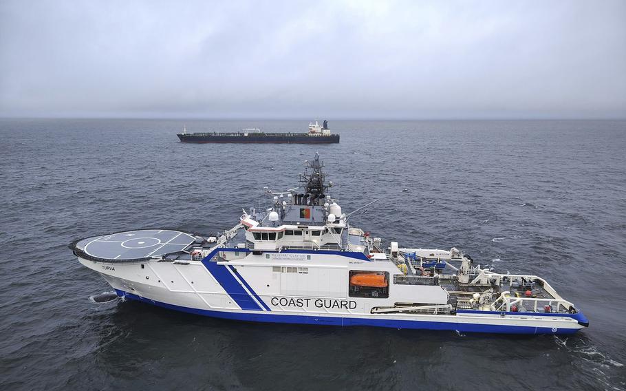 A white and blue Finnish coast guard ship in the foreground while the midground shows a gray tanker.