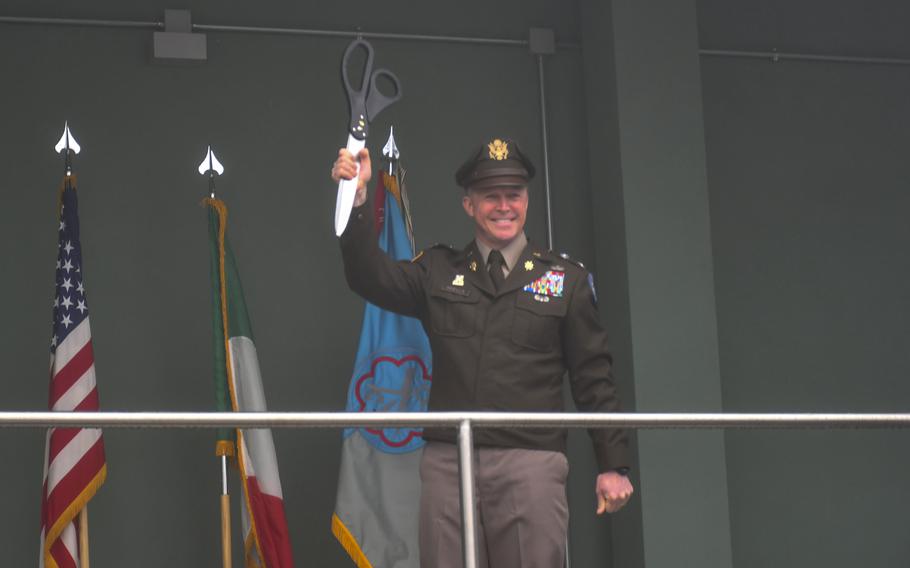 A man in uniform holds a giant pair of scissors above his head with one hand.