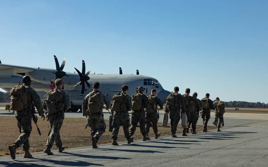 Marines march down a tarmac to board a plane.