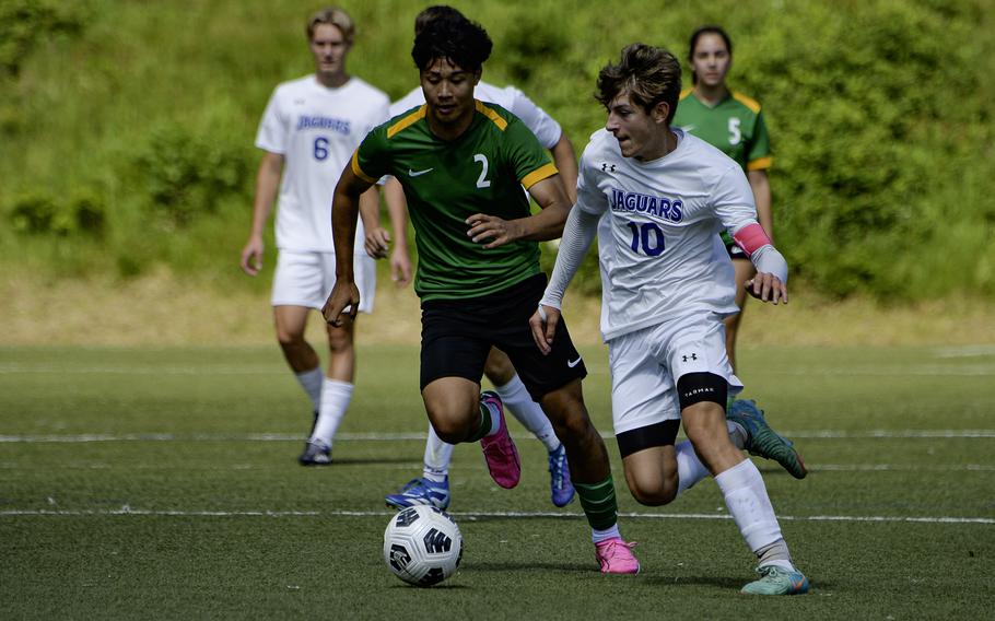 Boys in green and white uniforms chase a soccer ball.