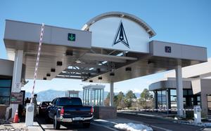 Cars lining up to a guarded entry gate above a metallic overhang with a Space Force logo.