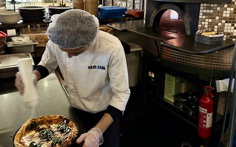 A chef at Melenzane restaurant in Manama, Bahrain, drizzles sauce over a barbecue pizza, one of the four pizzas offered. It is topped with smoked chicken, mushrooms and kale.