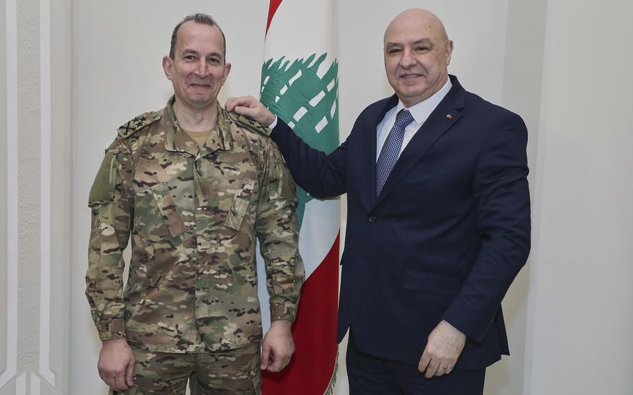 Two men, one in military fatigues and the other in a suit, smile for a picture.