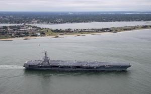 An aircraft carrier cruises past land.