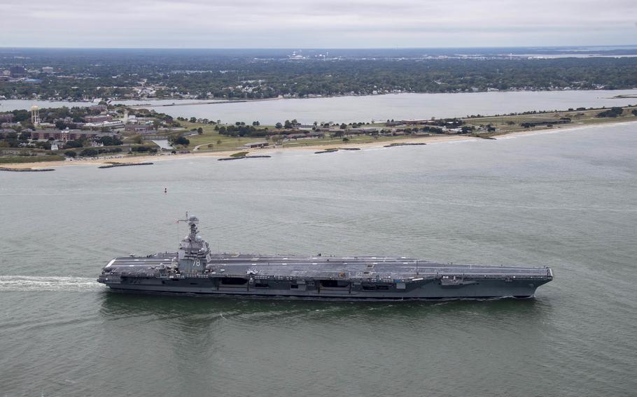 An aircraft carrier cruises past land.