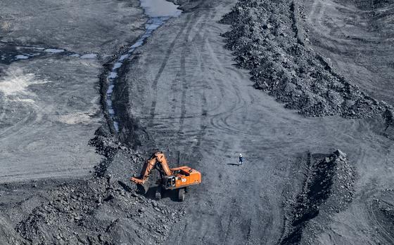 An orange mining vehicle, seen from above, sifts through a pile of rocks with a small figure visible near it.