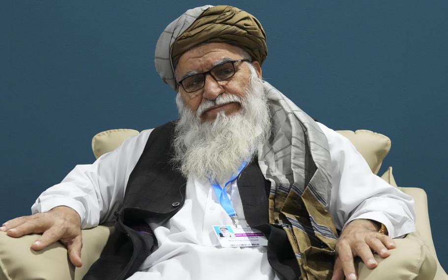 An Afghan man with a large white beard wearing a turban and glasses sits in an armchair.