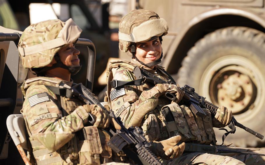 Two women seated in Army fatigues, holding rifles.