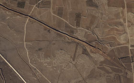 A satellite image shows an overhead view of a trench being dug in desert terrain.