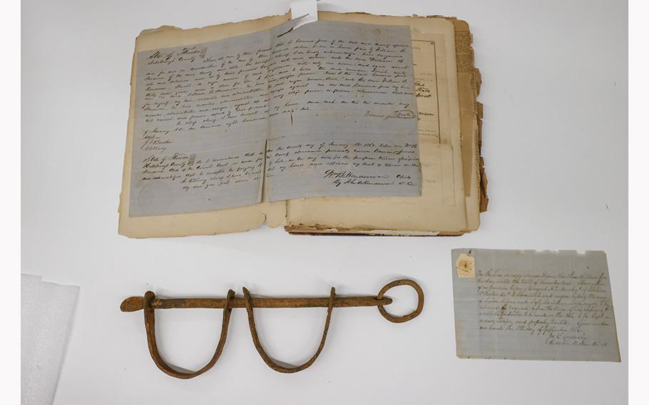 Slavery artifacts: shackles from the Spanish slave trade, bottom left, An enslavement contract, top, and a receipt from September 1856 for a one-year lease of enslaved woman Diana and her three enslaved children signed by Tampa’s first mayor Joseph B. Lancaster.