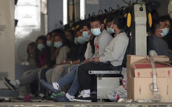 Migrants wearing face masks and shackles on their wrists and ankle sit in a row of seats on a military aircraft.