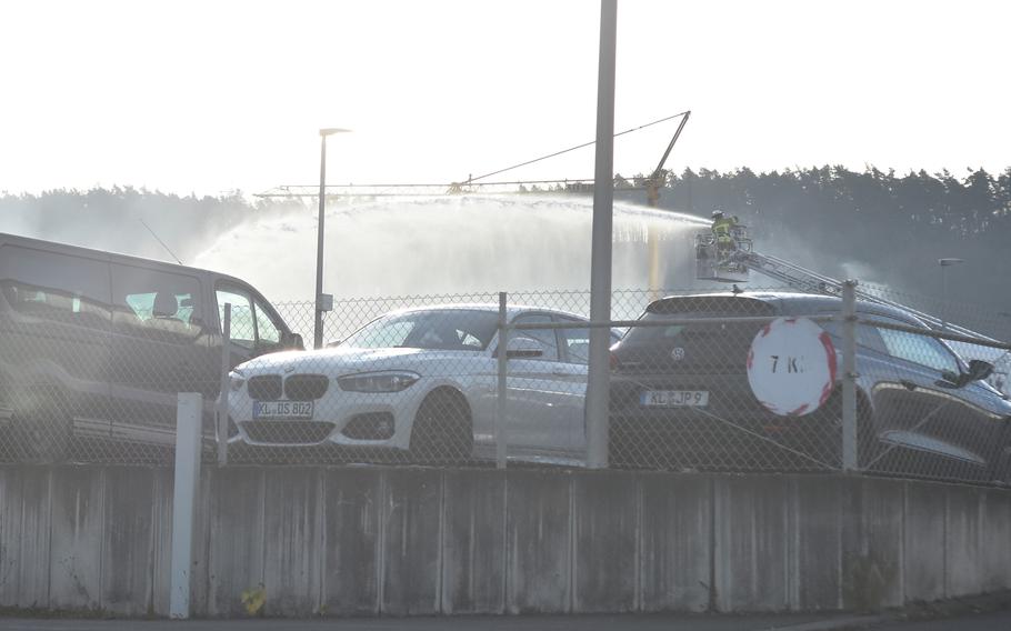 Parked cars in the foreground and a firefighter spraying water from an elevated bucket in the background.