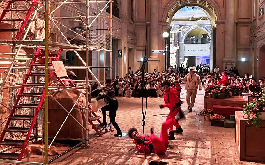 An audience watches performers on a theater stage with scaffolding.