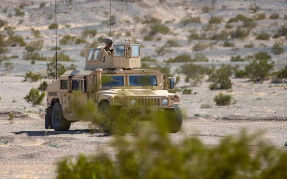 A Humvee is driven through desert terrain with a Marine standing in the gunner position.