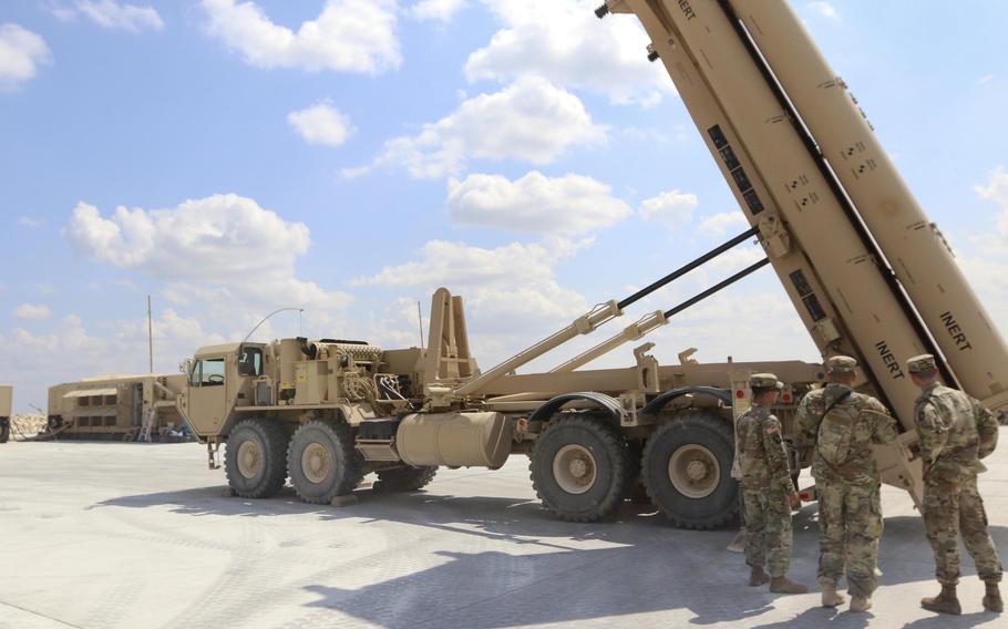 Soldiers stand in front of a missile defense system.