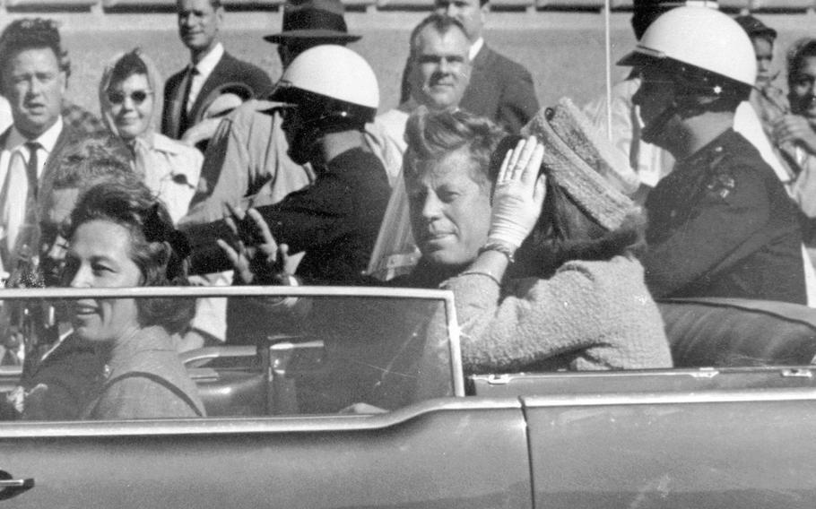 President John F. Kennedy waves from his car in a motorcade in Dallas, with first lady Jacqueline Kennedy, right.