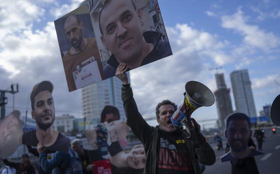 A protester speaks into a bullhorn and holds a sign with a photo of a freed hostage.