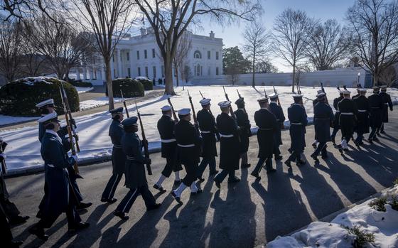 People in navy uniforms carrying bayonets march past the White House.