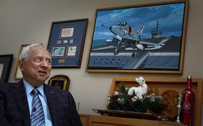 Retired Navy Cmdr. Everett Alvarez speaks during an interview while sitting in front of a picture of a Navy jet and other military memorabilia.