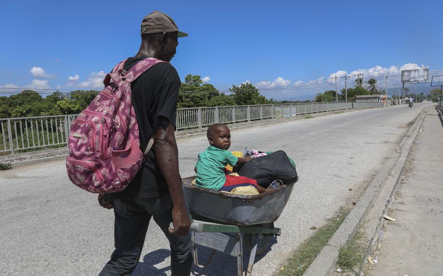 A man pushes a child in a wheelbarrow along a street 