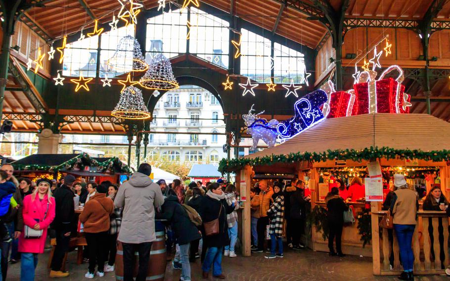 People walk among festively lit booths at an indoor Christmas market.