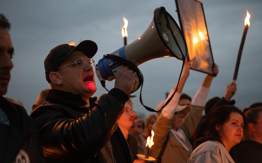 A man holds a megaphone and other protesters in the background hold torches and a sign that says “Justice for Micha.”